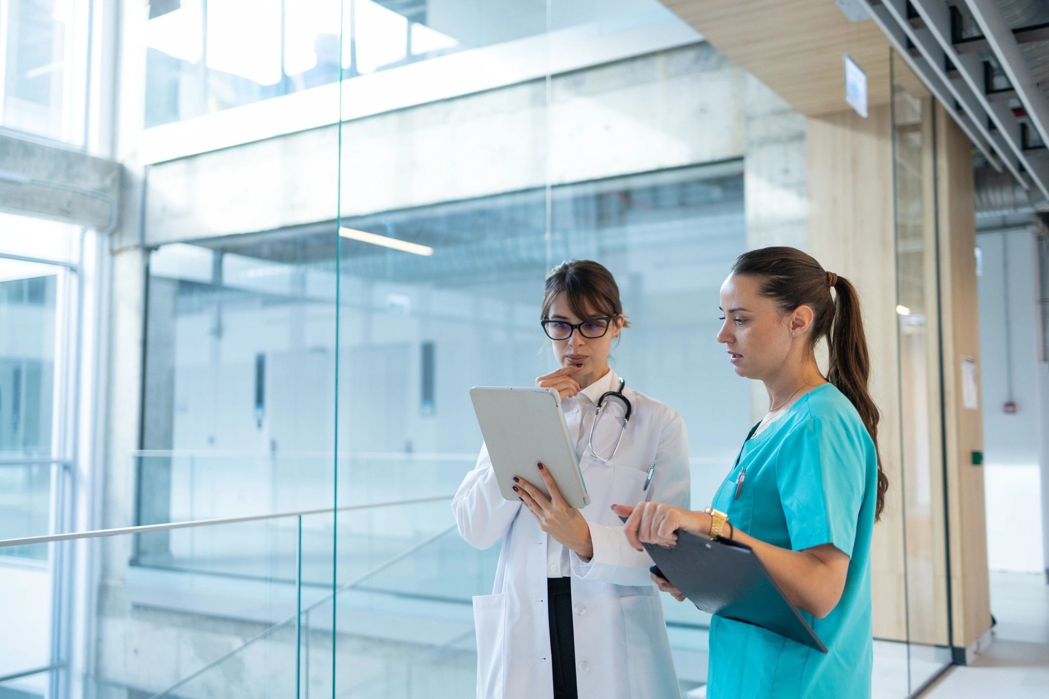 Two healthcare professionals reviewing tablet in hospital corridor
